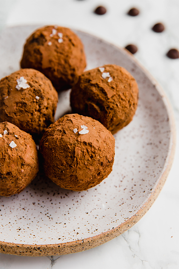 A white plate with five avocado truffles on it.