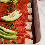 A white baking dish filled with paleo beef enchiladas topped with avocado slices.