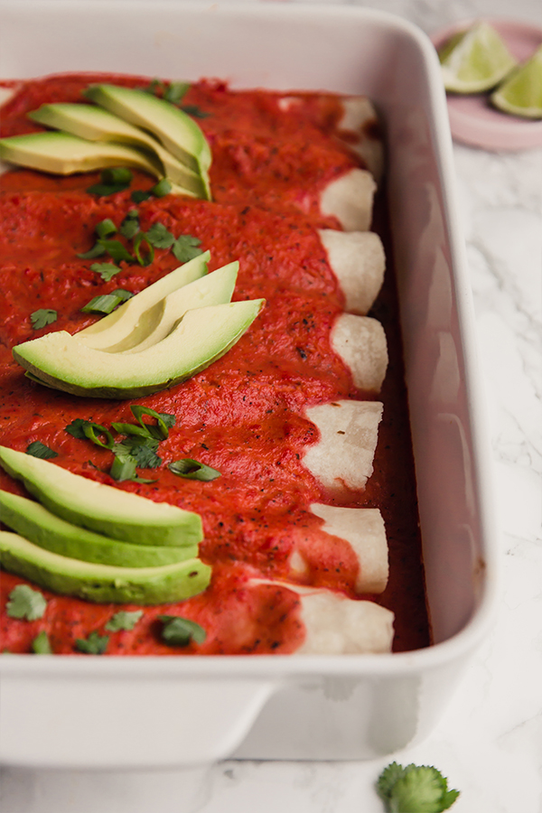 A white baking dish filled with paleo beef enchiladas topped with avocado slices.