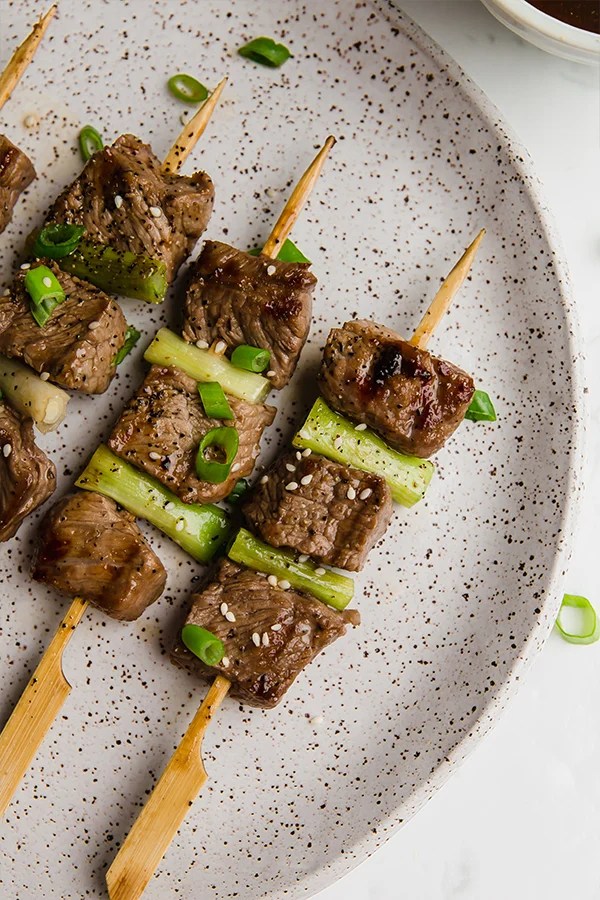 A ceramic plate with three Japanese inspired beef skewers on it.