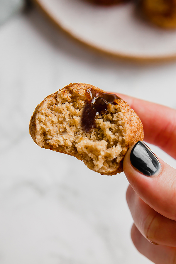 A hand holding a dulce de leche filled donut hole in it after a bite was taken out.