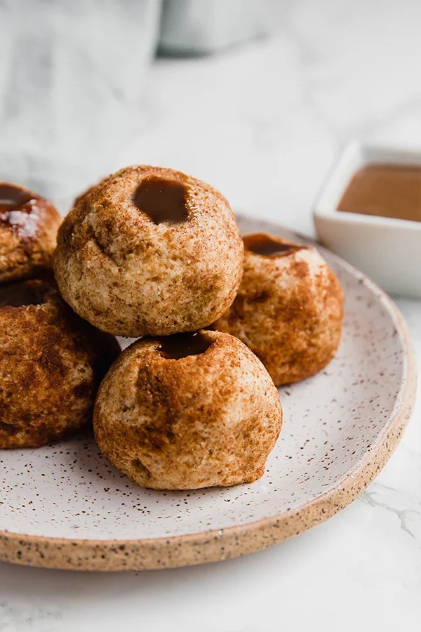 A plate with churro dulce de leche filled donut holes on it.