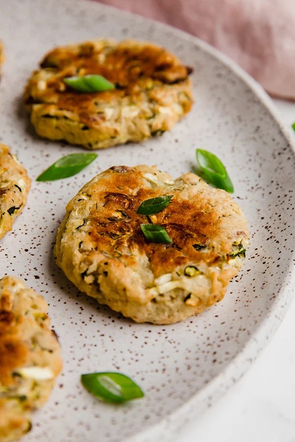 A bacon zucchini breakfast patty lying on a plate with extra herbs.