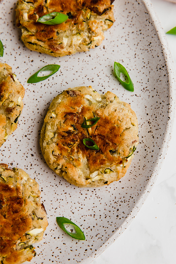 A bacon zucchini breakfast patty lying on a plate with extra herbs.
