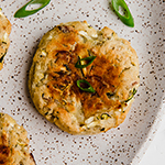 A bacon zucchini breakfast patty lying on a plate with extra herbs.