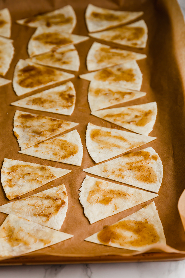 A baking sheet topped with parchment paper with cinnamon chips before being baked.