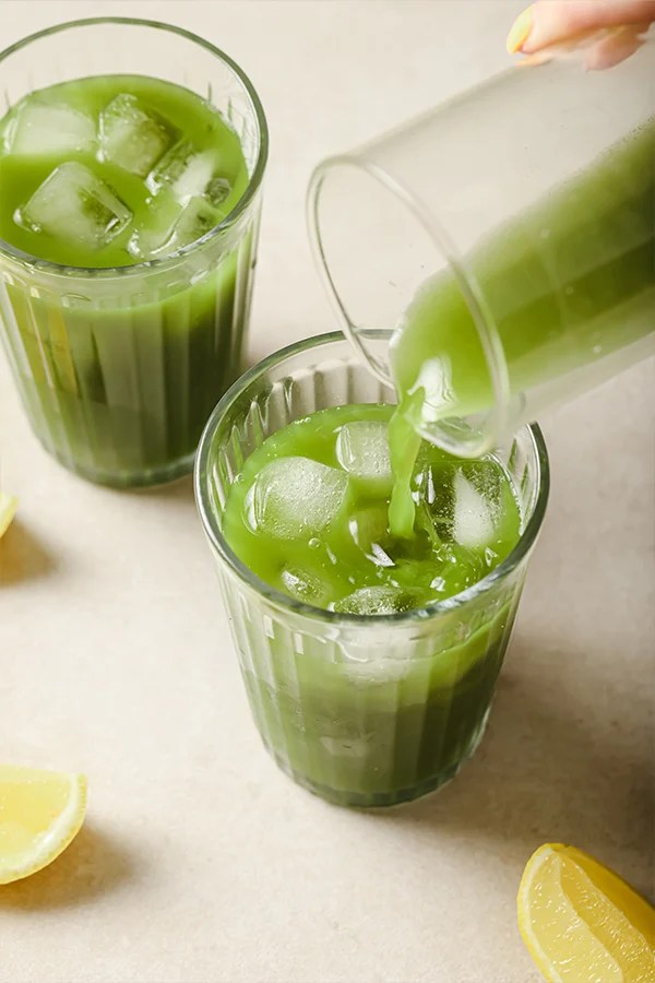 Matcha lemonade pouring into a glass with ice.