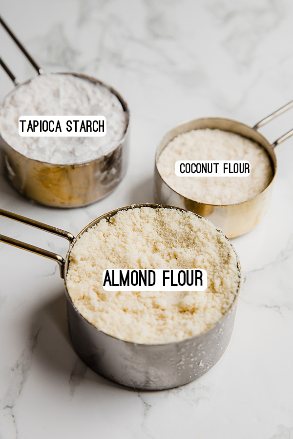 Measuring cups filled with different flours- tapioca starch, coconut flour, and almond flour.