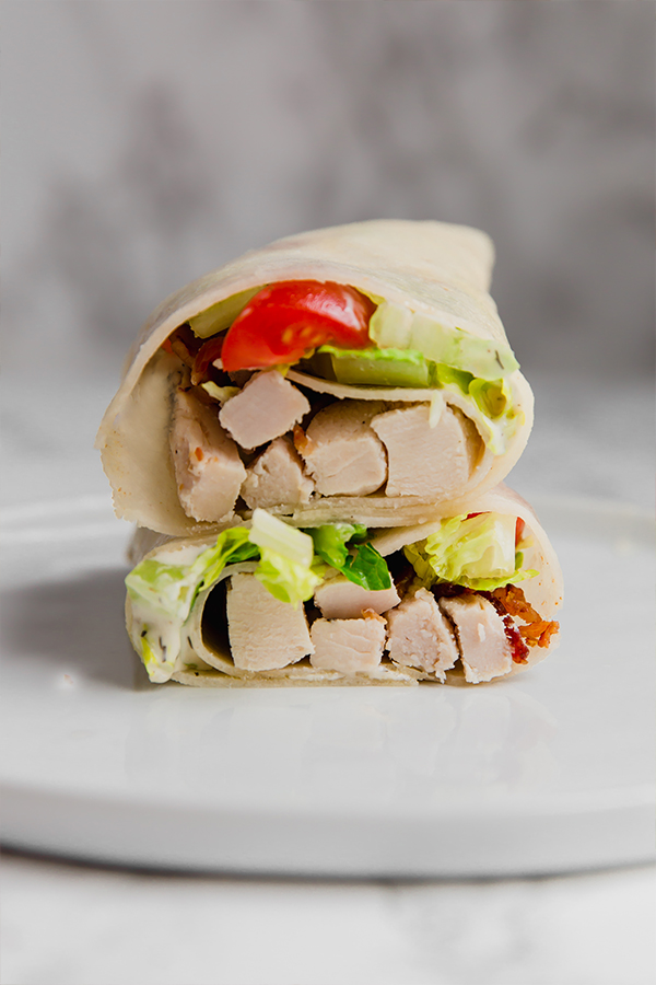A paleo chicken bacon ranch wrap cut in half with the two halves stacked on top of each other.