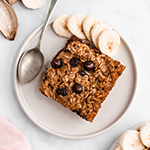 A white plate with a slice of chocolate banana baked oatmeal, sliced banana and a spoon.