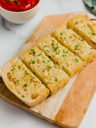 A loaf of gluten-free sourdough topped with garlic to make garlic bread cut into slices and on a wooden cutting board.