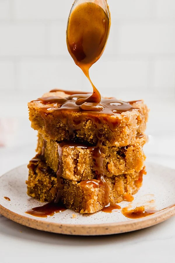 A stack of three salted caramel pumpkin blondies with caramel sauce being drizzled over it.