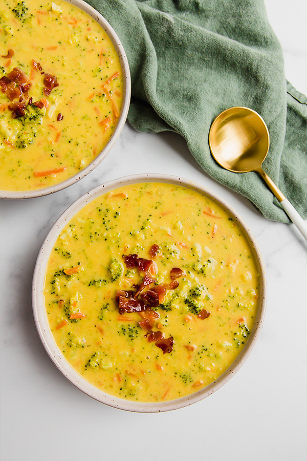 Two bowls of broccoli cheese soup with a green napkin