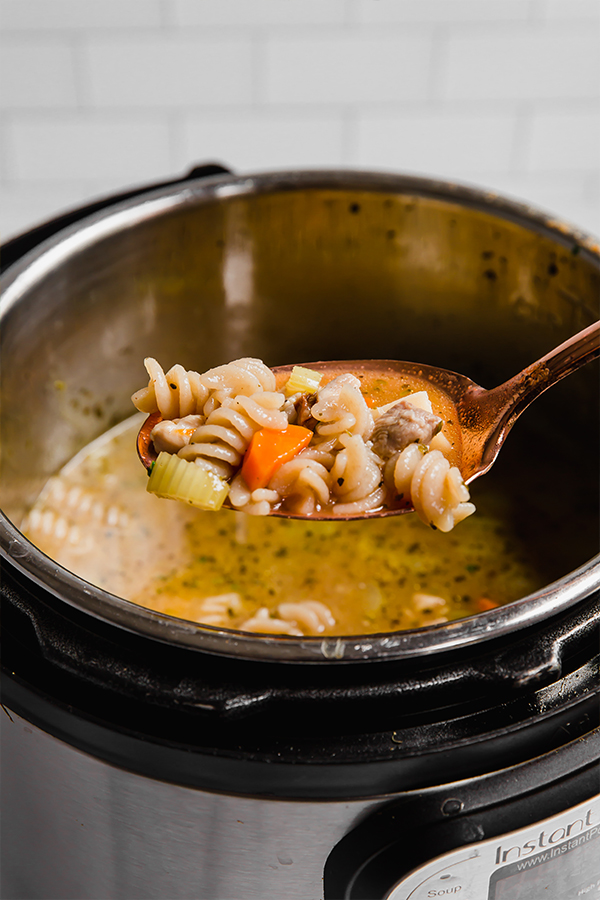 A instant pot with a serving spoon of chicken noodle soup being scooped out.