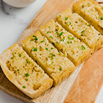 A loaf of gluten-free sourdough topped with garlic to make garlic bread cut into slices and on a wooden cutting board.