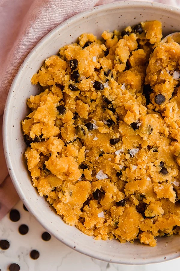 A white bowl filled with edible pumpkin chocolate chip cookie dough.