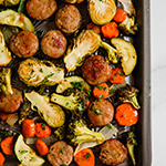 A sheet pan with sausage and vegetables being roasted.
