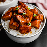 A white bowl with cauliflower rice topped with paleo general tso's chicken.