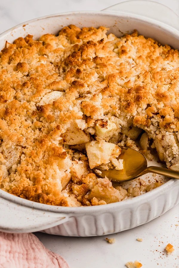 Apple crisp in a pan with a spoon scooping a serving.