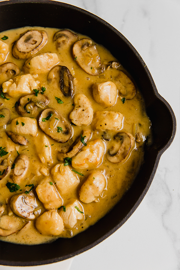 Chicken strogranoff with mushrooms and sauce in a black pan.