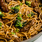 Gluten free and broccoli lo mein topped with green onions and sesame seeds in a pan topepd with sesame seeds.