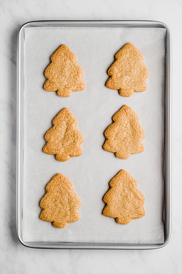 A sheet pan with six christmas three sugar cookies after baking.