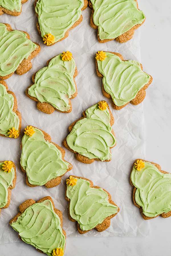 Many sugar cookies shaped like a Christmas tree with green icing and a yellow icing star on top.