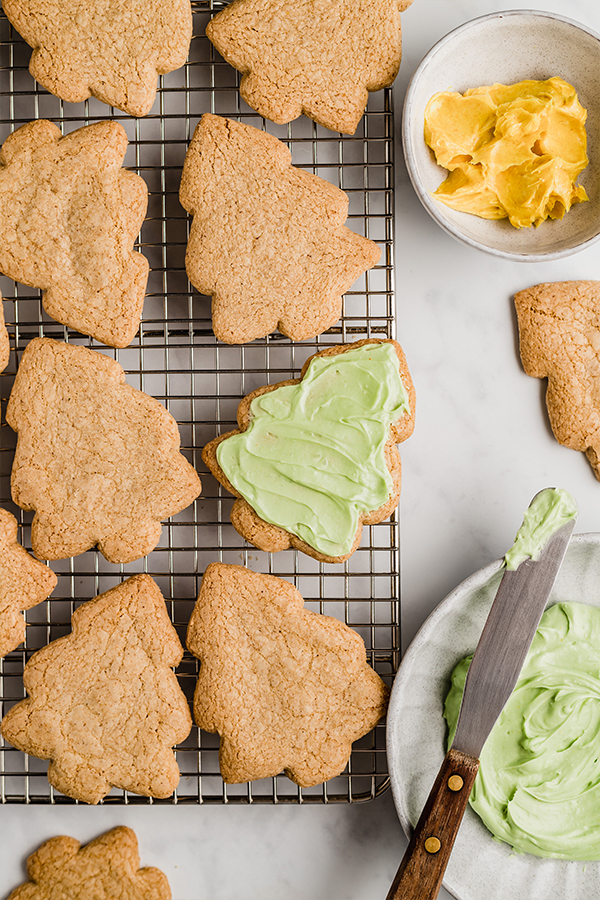 A wire rack topped with christmas tree sugar cookies with one iced with green icing.