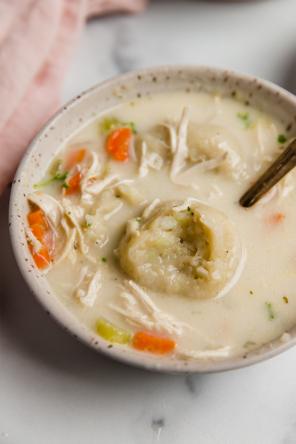 Gluten free chicken and dumplings in a bowl topped with parsley, with a dumpling with a bite.