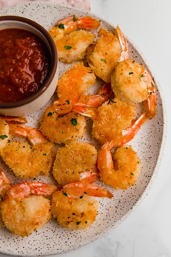 Oven baked coconut shrimp on a plate with a side of sauce.