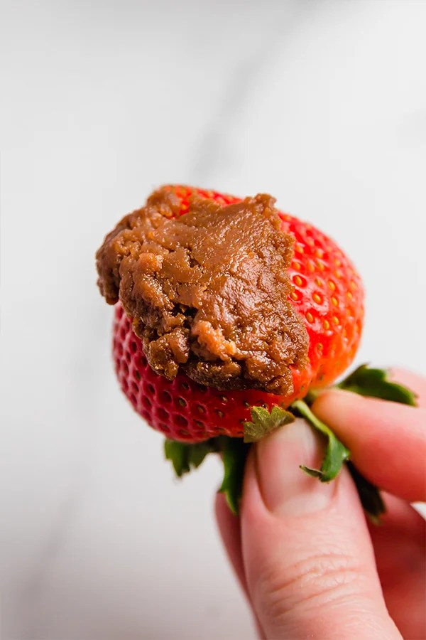 A strawberry being held with cookie butter.