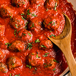 Oven baked meatballs in a pan with a wooden spoon topped with parsley.