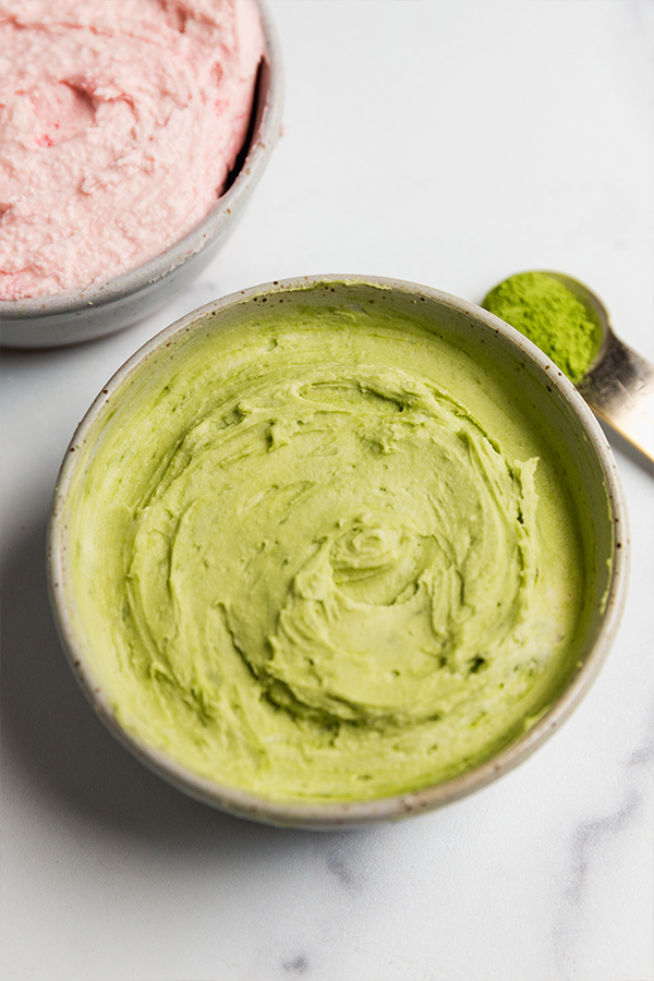 Green frosting in a bowl with matcha powder on the side.