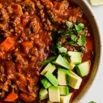 Beef and bacon chili in a bowl topped with avocado and cilantro.