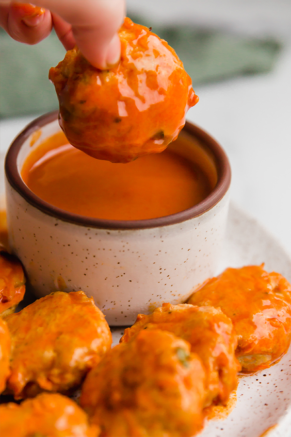 Buffalo chicken poppers on a plate with one being dipped into sauce.