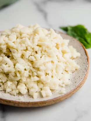Shredded dairy free cheese on a plate with basil in the background.