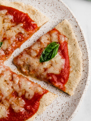 Tigernut flour pizza slice on a plate topped with a piece of basil.