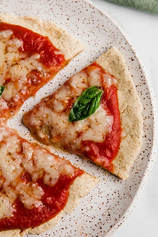 Tigernut flour pizza slice on a plate topped with a piece of basil.
