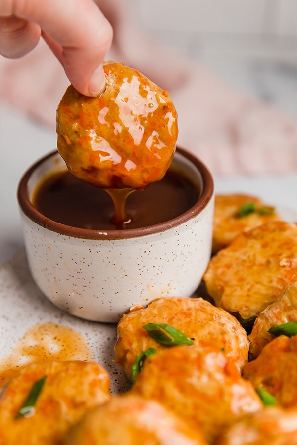 Sweet and soup chicken poppers on a plate with one being dipped in sauce.