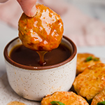 Sweet and soup chicken poppers on a plate with one being dipped in sauce.