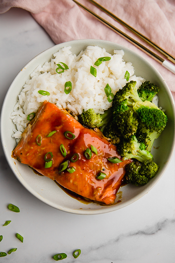 teriyaki salmon bowl with broccoli and rice, chopsticks on the side