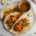 Three thai chicken tacos on a plate with sauce on the side.