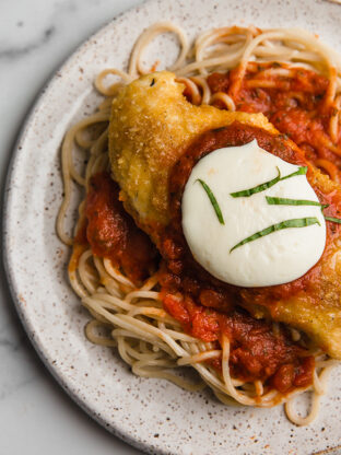 Chicken parmigiana over noodles on a plate.