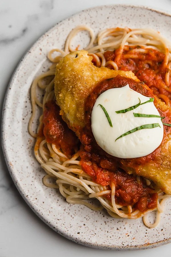 Chicken parmigiana over noodles on a plate.