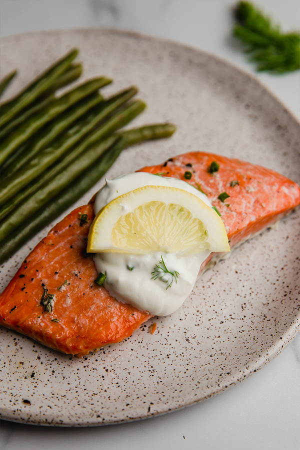baked salmon with creamy lemon dill sauce on plate with green beans and lemon wedge