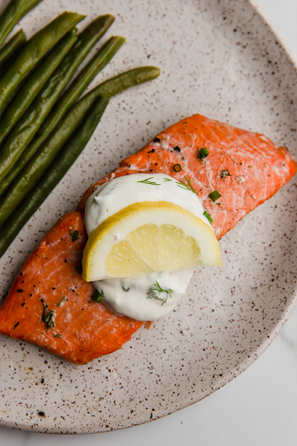 Baked salmon topped with creamy lemon dill sauce and a lemon slice.