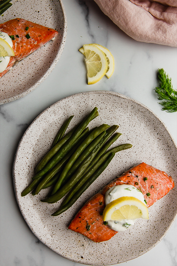 Baked salmon topped with creamy lemon dill sauce on a plate with beans.