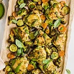 Chicken pesto with vegetables on a lined sheet pan.
