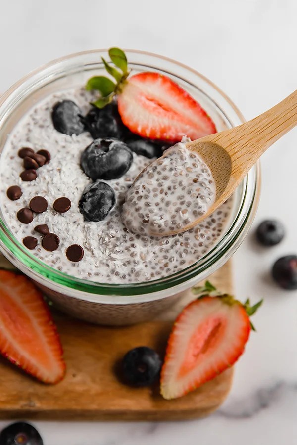 Close up top view of chia pudding in jar with berries and wooden spoon