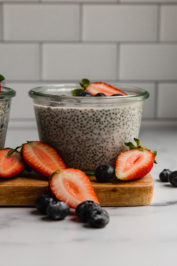 Side view of chia pudding in a jar with berries on top and displayed around